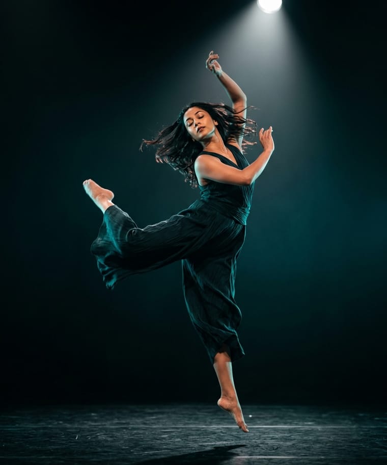 A contemporary dancer mid-leap under a stage spotlight